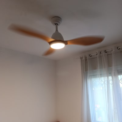 מאוורר תקרה עם תאורה בחדר שינה ליד חלון עם וילון לבן