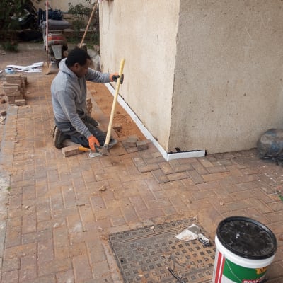 אדם עובד על ריצוף עם כלי עבודה ודלי איטום