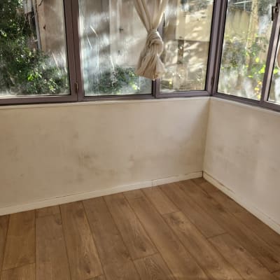 קיר לבן עם סימני לכלוך, רצפת עץ, חלונות עם וילונות קשורים