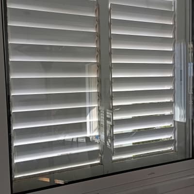 חלון עם תריסים לבנים פתוחים למחצה