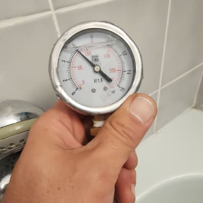 מד לחץ מים מוחזק ביד ליד ברז