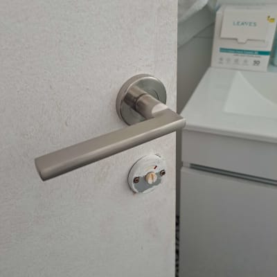 ידית דלת מתכתית על דלת לבנה בחדר אמבטיה