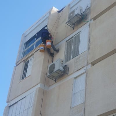 אדם מטפס על בניין עם ציוד עבודה בגובה