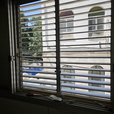 תריסים פתוחים עם נוף של בניין ועצים בחוץ