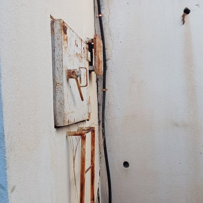 דלת מתכת חלודה, צינור שחור, פסולת על הקרקע