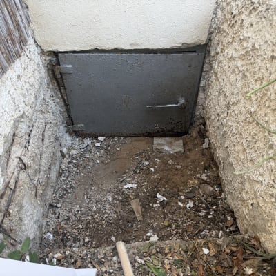 דלת מתכת ישנה בקיר חיצוני עם אדמה מסביב