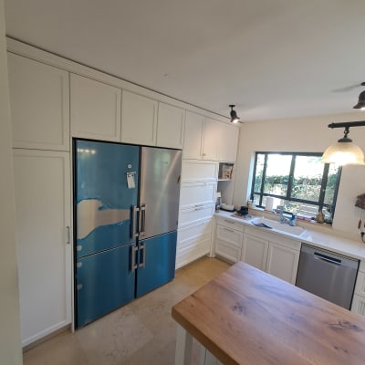 מטבח עם מקרר כחול, ארונות לבנים ושולחן עץ