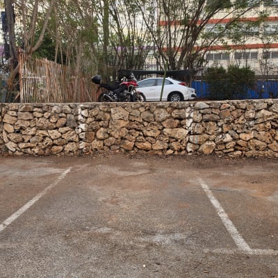חניון אספלט עם סימוני חנייה וקיר אבנים ברקע