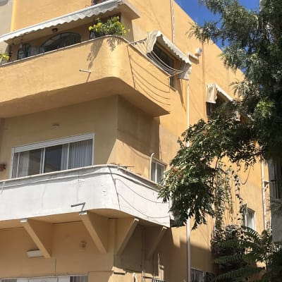 אדם עובד בגובה על בניין צהוב עם ציוד בטיחות