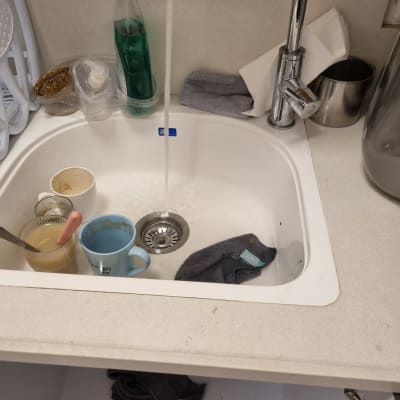 כיור עם כלים מלוכלכים וברז מים זורם