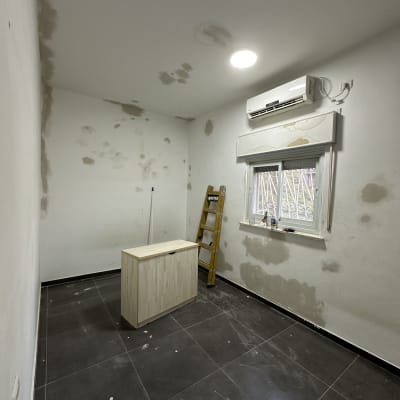 חדר עם קירות מוכנים לצביעה, סולם ועץ.