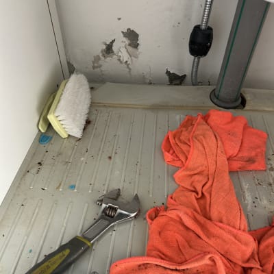 מברג, מברשת, סמרטוט כתום וכלי עבודה ליד צינור מים