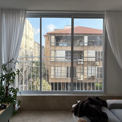 חלון גדול עם וילונות לבנים ודירה מולו