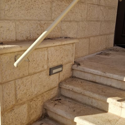 מאחז יד ממתכת מותקן על קיר אבן לצד מדרגות כניסה