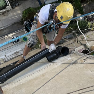 עובד בגובה עם קסדה צהובה מתקין צינור שחור