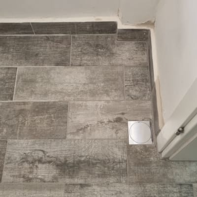 רצפת אריחים עם פתח ניקוז עגול בפינה