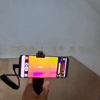 אדם מחזיק מצלמה תרמית לבדיקת נזילות בקיר