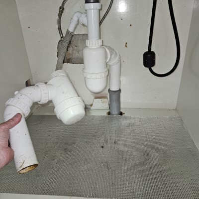 תמונה של צנרת מתחת לכיור עם יד מחזיקה חלק