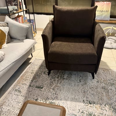 כורסה חומה על שטיח מעוצב בסלון עם מדף ספרים.