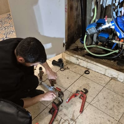 אדם מתקן צנרת עם כלים מתחת לכיור