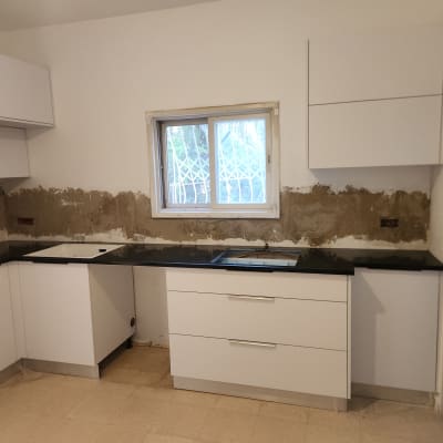 מטבח בשיפוץ עם ארונות לבנים וקיר לא גמור