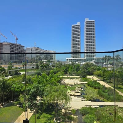 מעקה זכוכית עם נוף לגינה ומגדלים ברקע