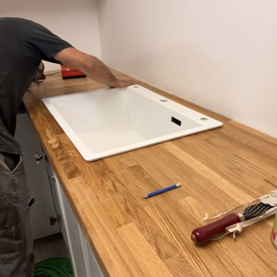 אדם מתקין כיור על משטח עץ במטבח