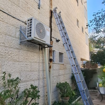 סולם ליד קיר עם מזגן חיצוני, צמחייה מסביב