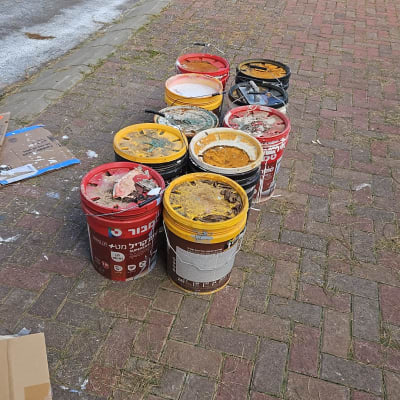 דלי צבעים ריקים על מדרכה ליד פח ירוק