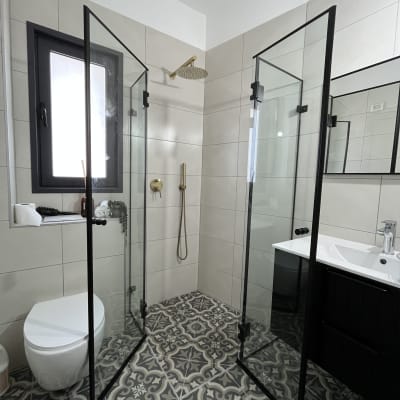 מקלחון זכוכית עם ראש מקלחת מוזהב ורצפת אריחים מעוצבת