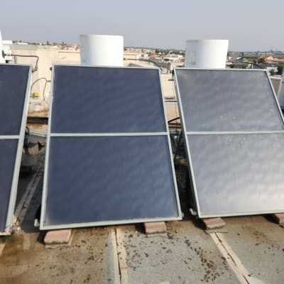 קולטי שמש מותקנים על גג שטוח עם דודים לבנים.