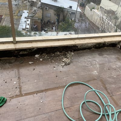 מרפסת עם רצפה שבורה, צינור ירוק ופסולת בנייה