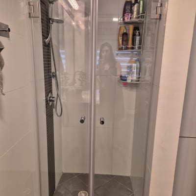 מקלחת עם דלתות זכוכית ומדף מוצרי טיפוח