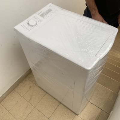 מכונת כביסה עטופה בניילון על רצפה ליד מדרגות