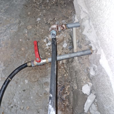 צינור מתכת עם ברז אדום ליד קיר בטון