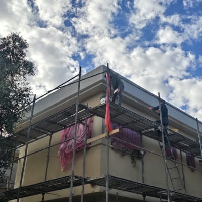 עובדים על פיגומים צובעים מבנה תחת שמיים מעוננים