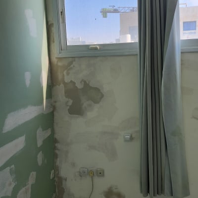 קיר עם טיח מתקלף ליד חלון עם וילון