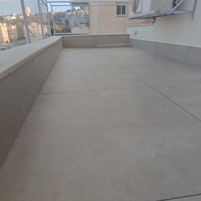 מרפסת מרוצפת עם מעקה זכוכית ומזגן על הקיר