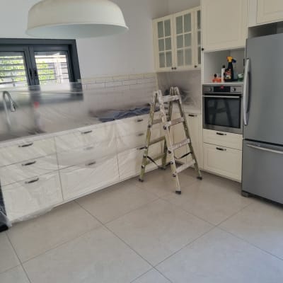 הכנה לצביעת מטבח מרוהט הכוללת כיסוי ארונות בניילון וסולם עבודה
