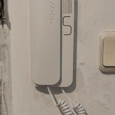 אינטרקום לבן עם כפתור ושפופרת תלויה על הקיר