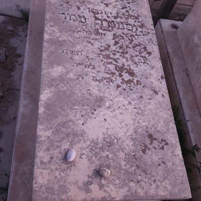 מצבה עם כיתוב בעברית ואבנים קטנות מונחות עליה