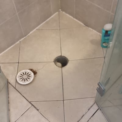 רצפת מקלחת עם פתח ניקוז פתוח ומכסה מונח בצד