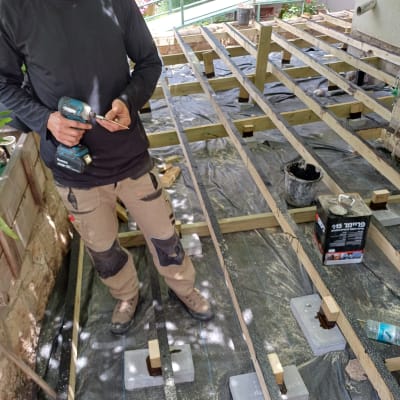 אדם מחזיק מברגה ליד מבנה עץ בגינה