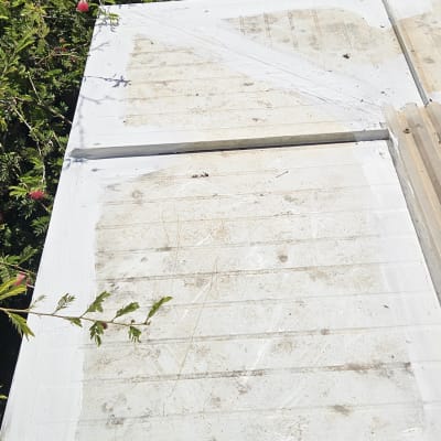 לוח עץ צבוע לבן עם צמחייה ברקע