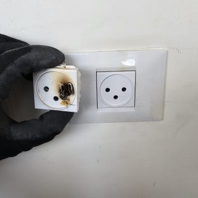 שקע חשמלי שרוף מוחזק על ידי כפפה שחורה