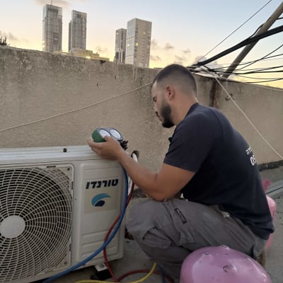 טכנאי בודק מזגן על גג עם בלוני גז