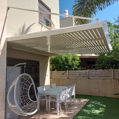 פרגולה לבנה מעל שולחן וכיסאות בגינה