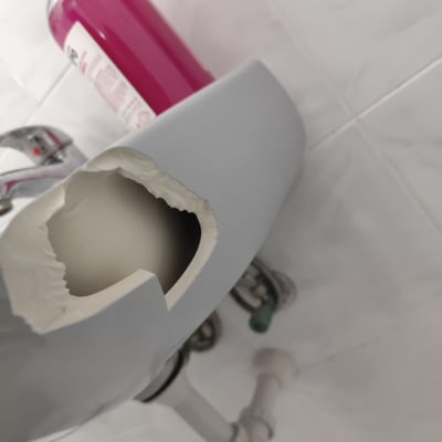 כיור שבור עם סבון נוזלי ורוד על רקע קיר קרמיקה.