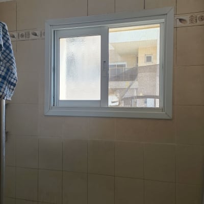 חלון הזזה עם מסגרת לבנה על קיר אריחים