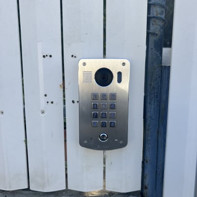 אינטרקום מותקן על גדר לבנה עם לוח מקשים ומצלמה